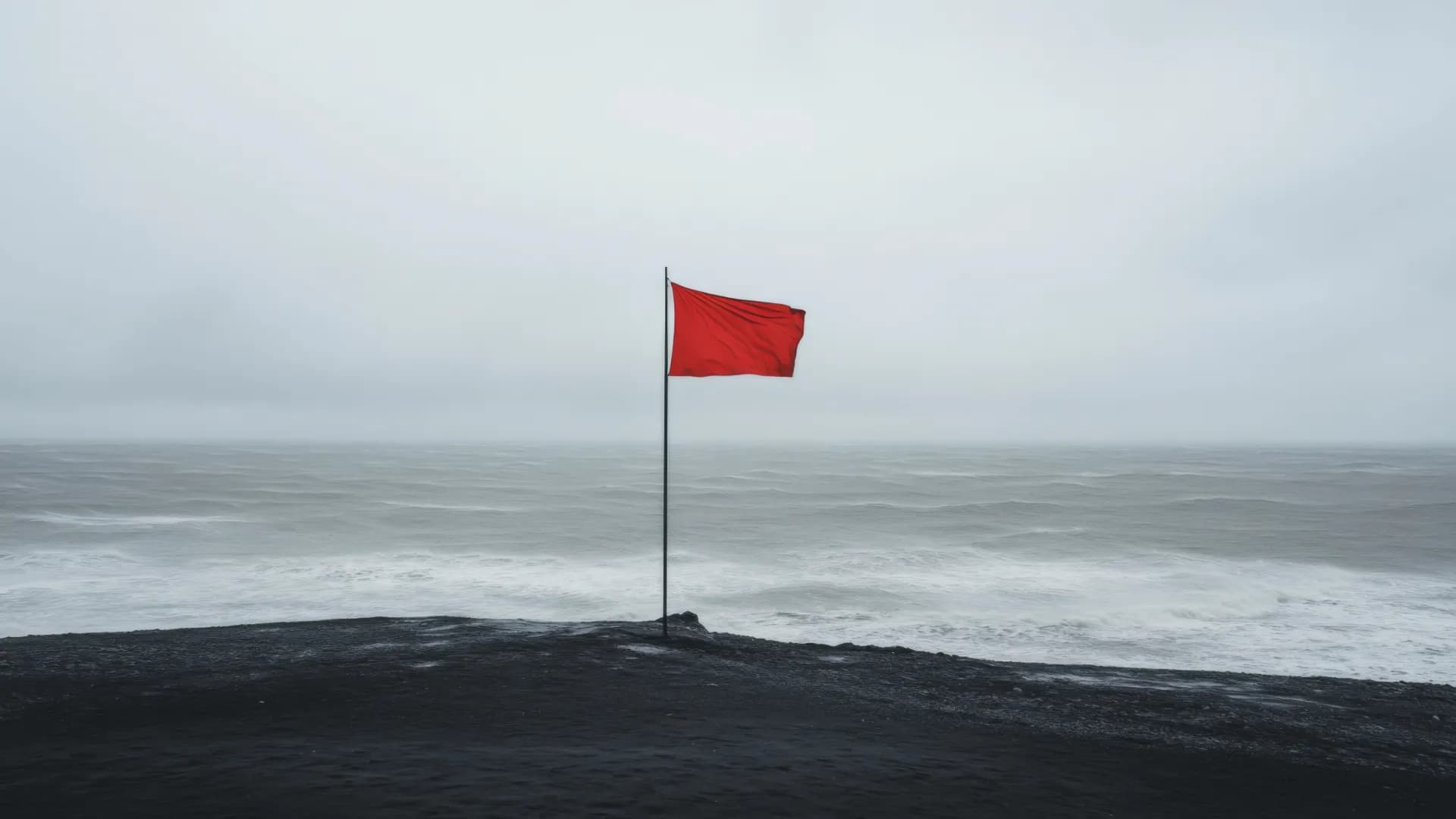 Röd flagga på klippa framför stormigt hav.